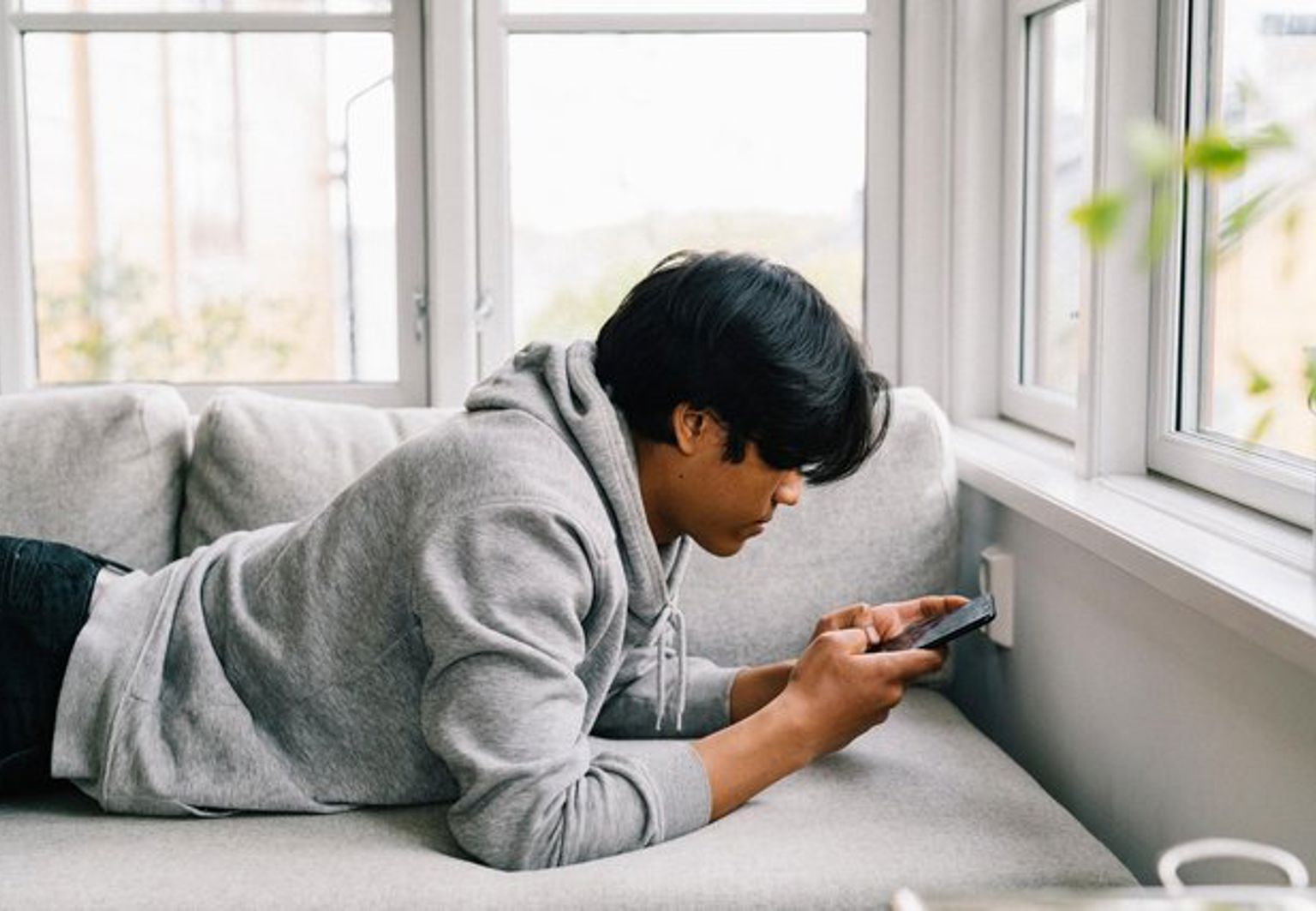 Tonåring surfar på sin telefon i soffan