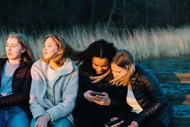 Fyra tonårsflickor sitter med telefonen utomhus