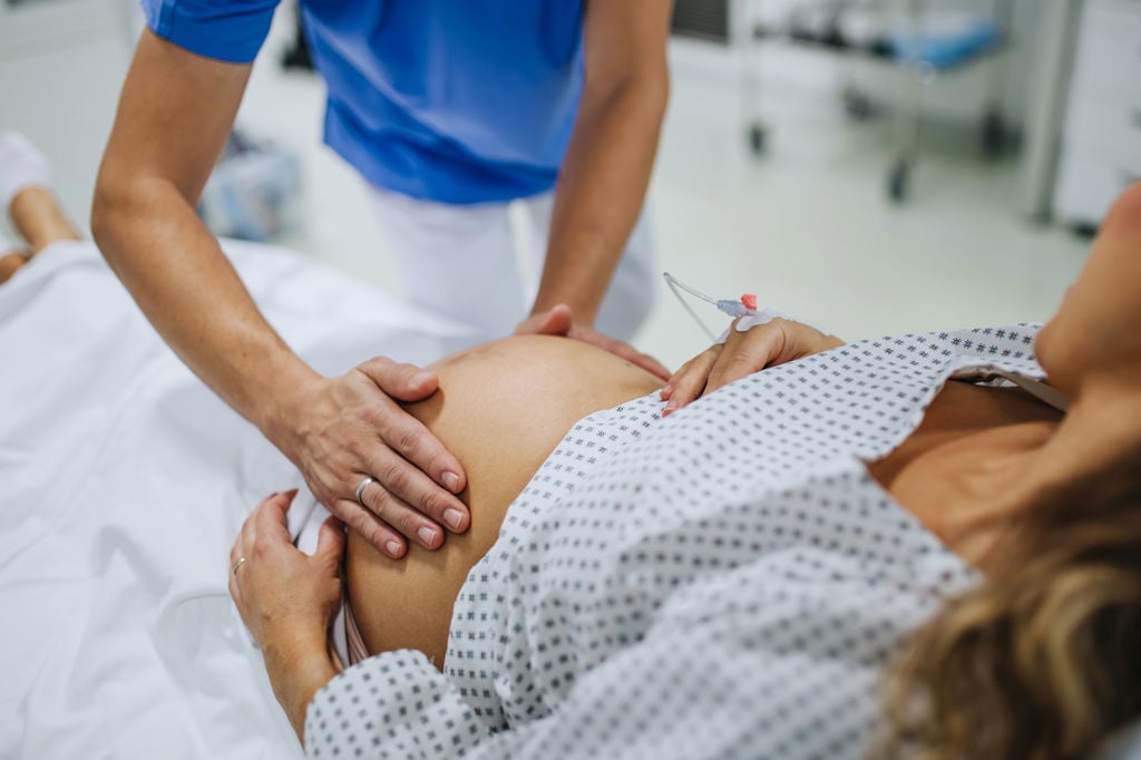 Barnmorska håller händerna på en gravid kvinnas mage inne i ett förlossningsrum