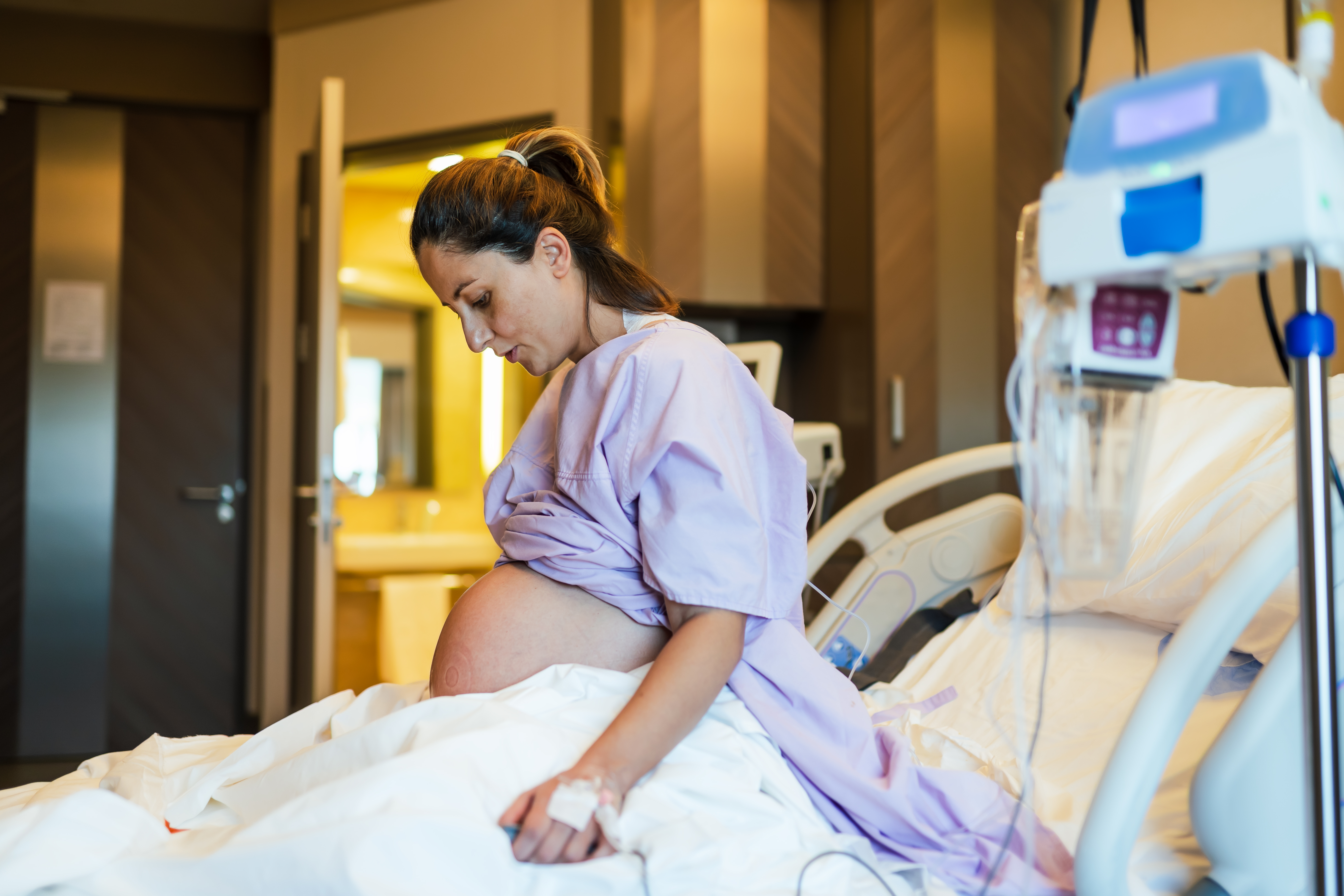 Gravid kvinna sitter i en säng på förlossningen