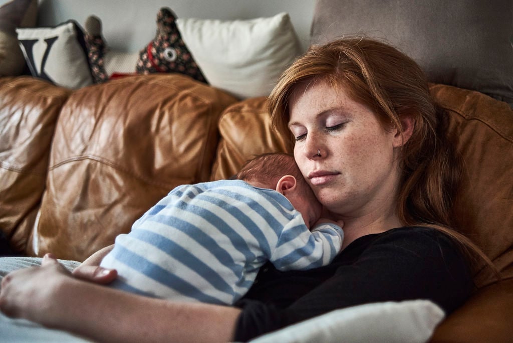 kvinna vilar i en soffa med sin bebis i famnen