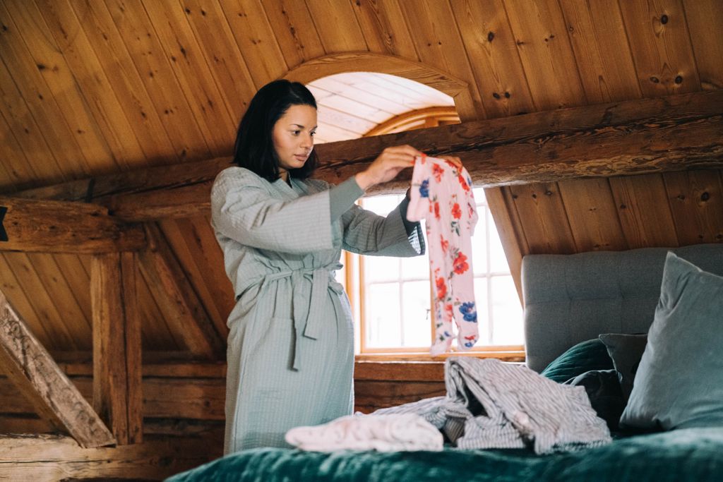 gravid kvinna i grå morgonrock viker tvätt på en säng