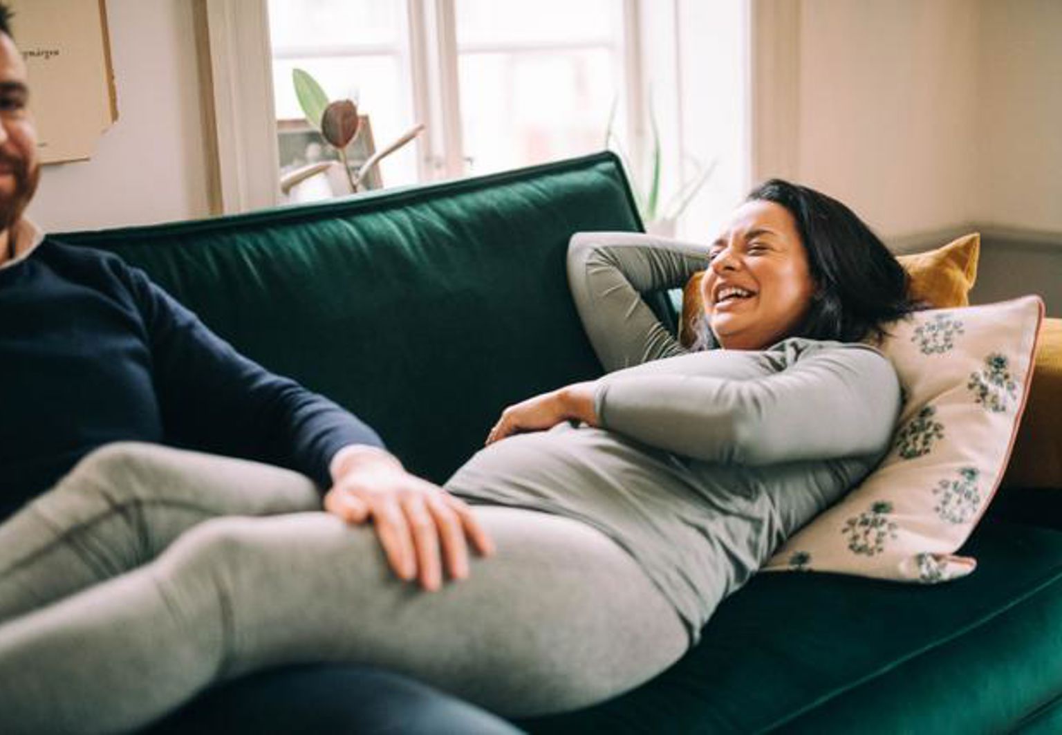 Gravid kvinna ligger i soffan och skrattar bredvid en man