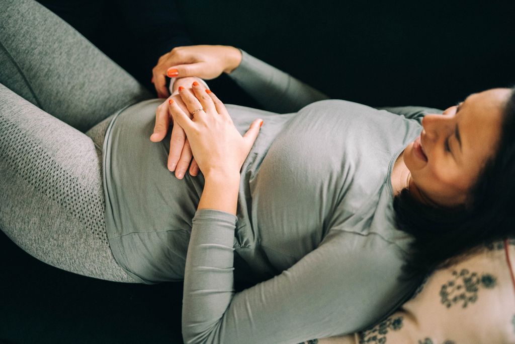 gravid kvinna i grå kläder ligger i en soffa