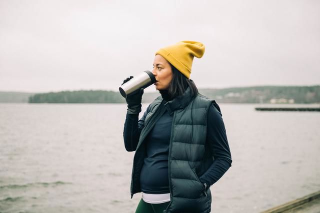 Gravid kvinna är ute på promenad och dricker ur en termos