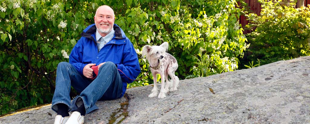 En man med ett stort leende sitter på ett berg med sin hund