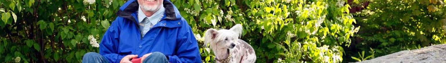 En man med ett stort leende sitter på ett berg med sin hund