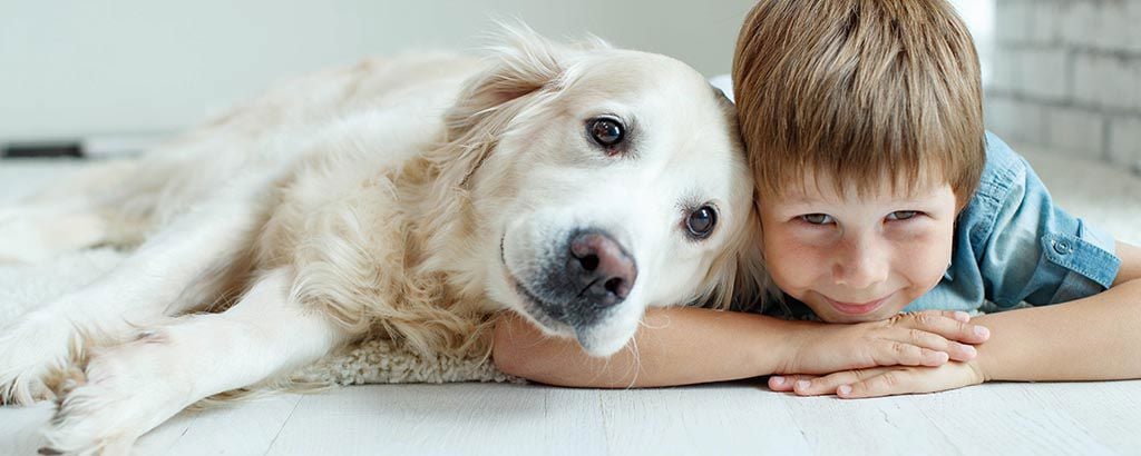 Nöjd pojke ligger på mage på golvet med en hund tätt intill.