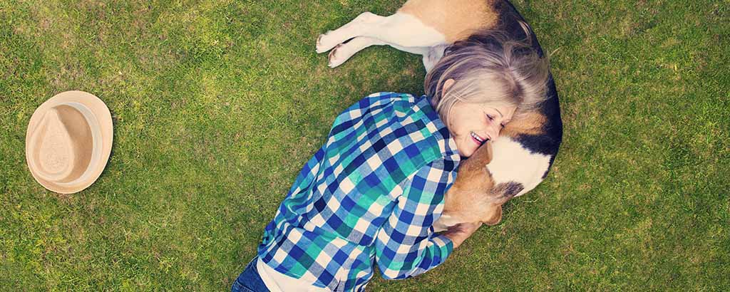 Kvinna och hund kramas liggandes på en gräsmatta