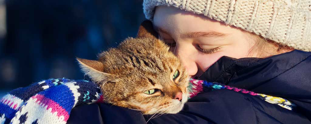 Ett barn med halsduk och mössa är glad och kramar om sin katt