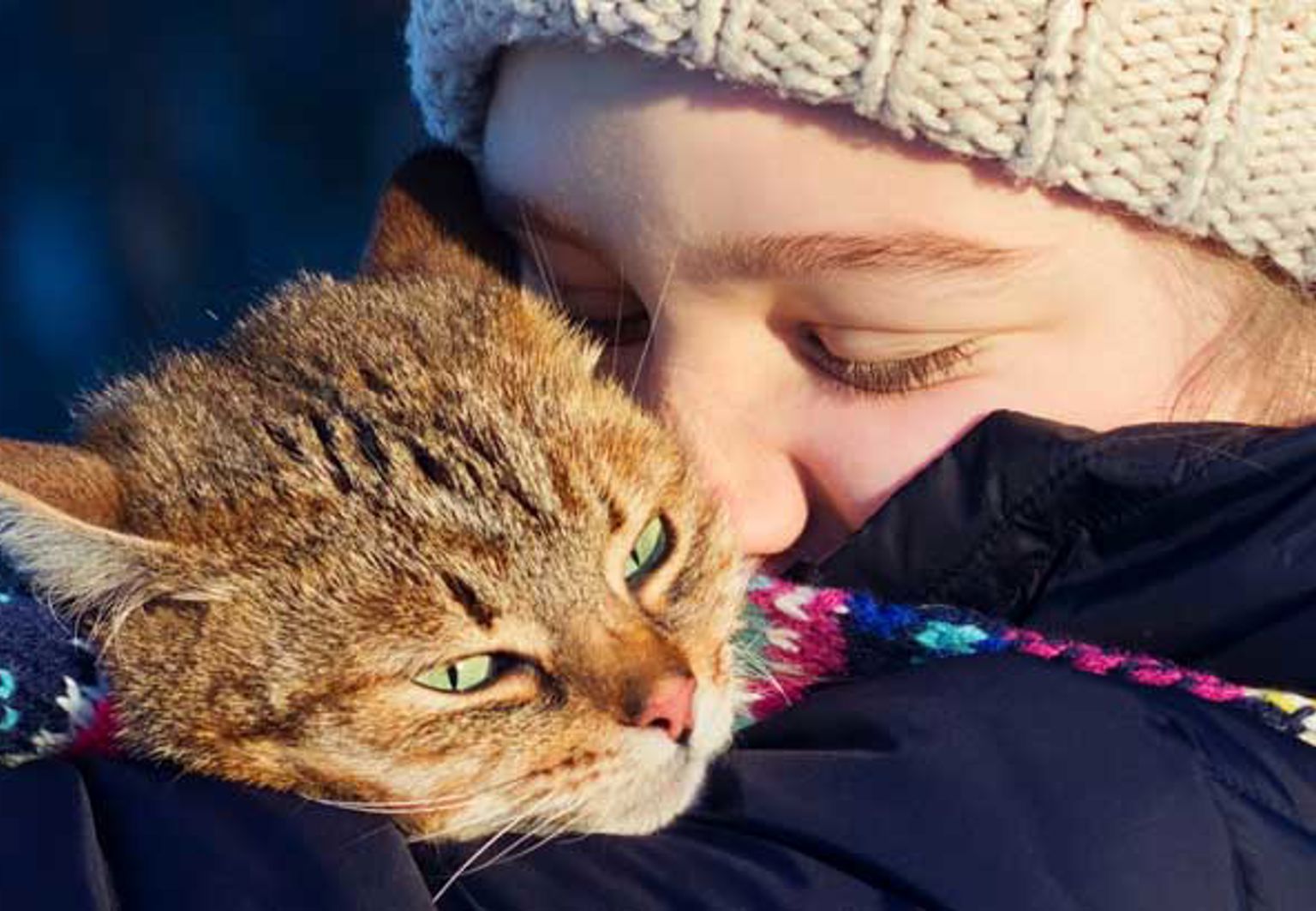 Ett barn med halsduk och mössa är glad och kramar om sin katt
