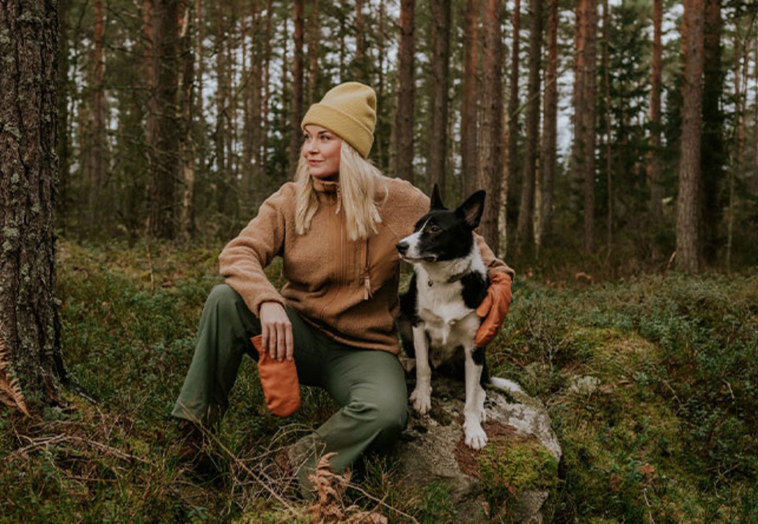 kvinna och border collie sitter på en sten i skogen