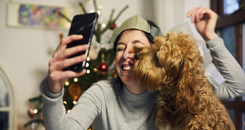En kvinna tar en selfie med sin hund med en julgran i bakgrunden