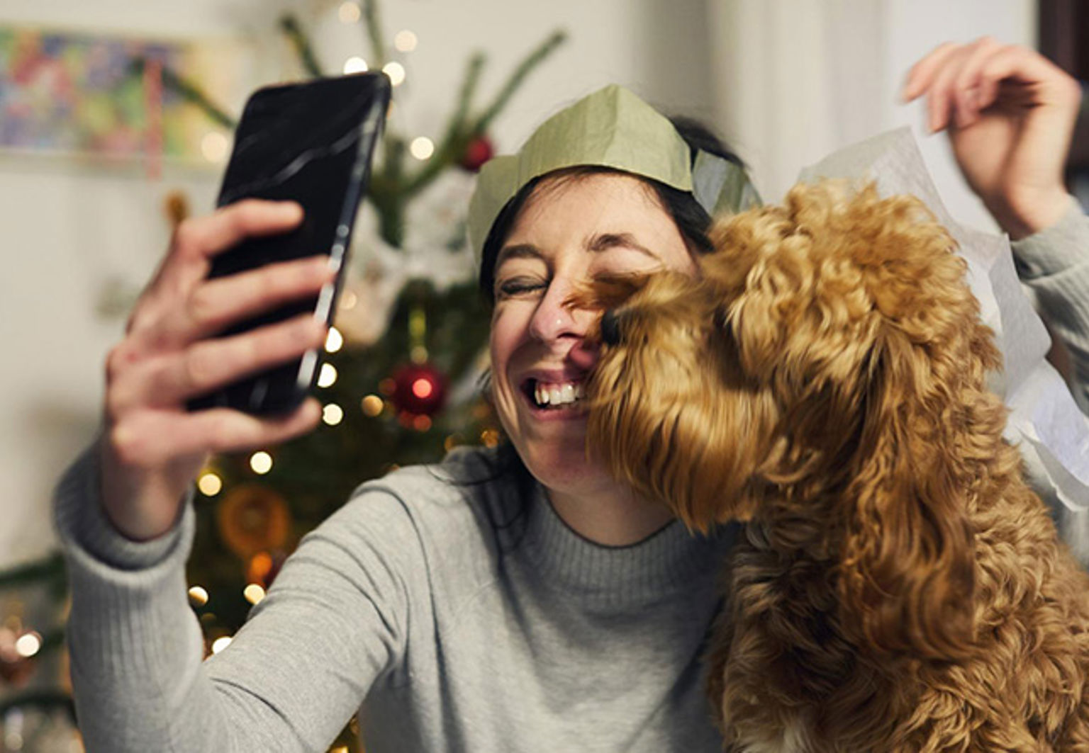 En kvinna tar en selfie med sin hund med en julgran i bakgrunden