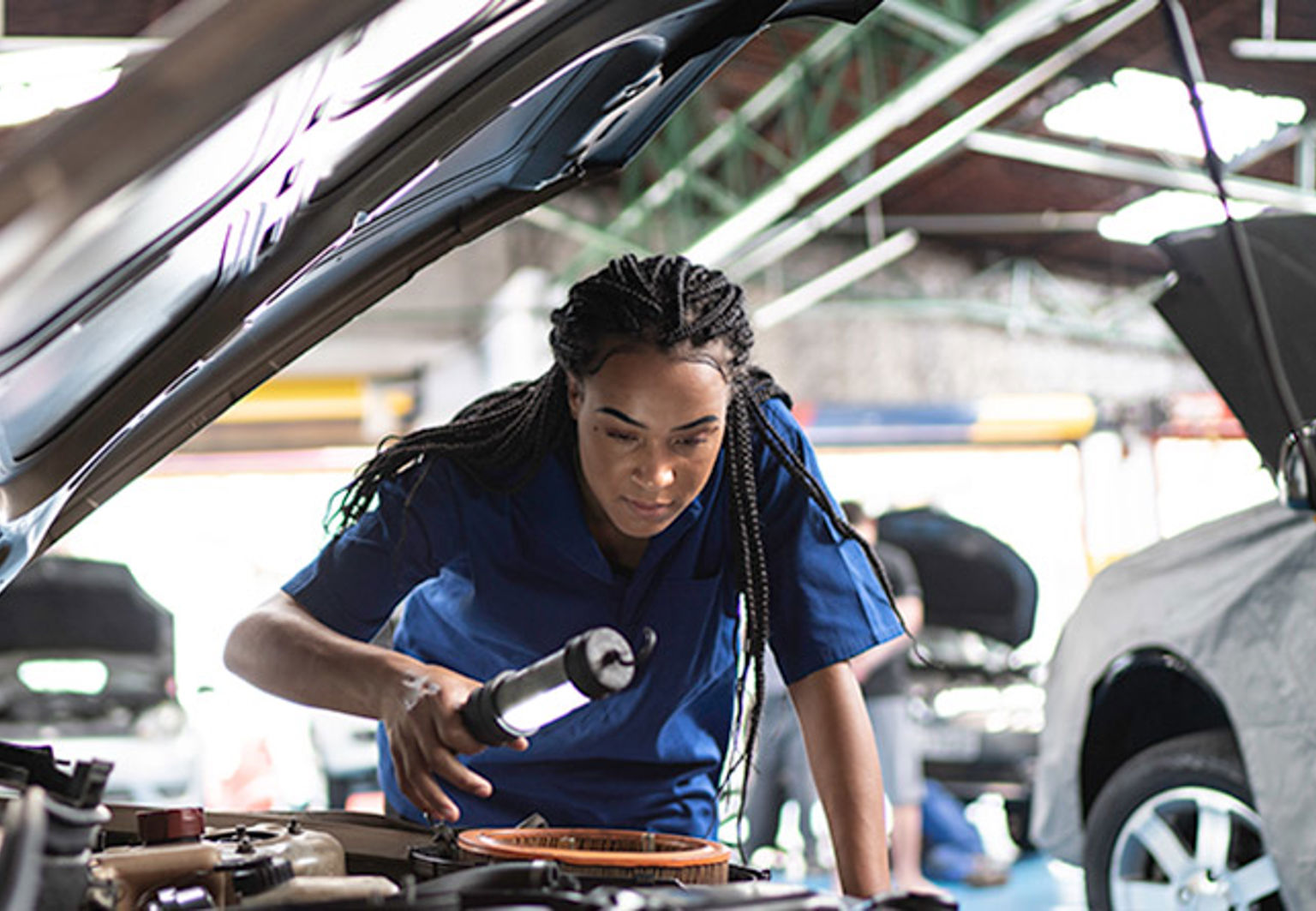 ung tjej bilmekaniker kollar under huven på en bil