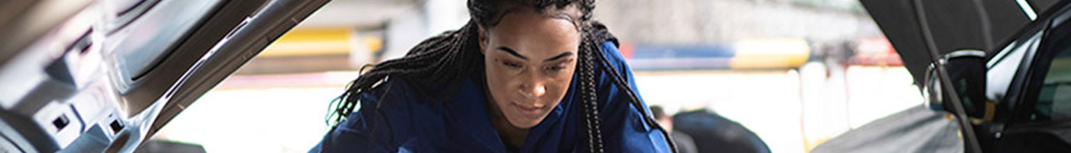 ung tjej bilmekaniker kollar under huven på en bil