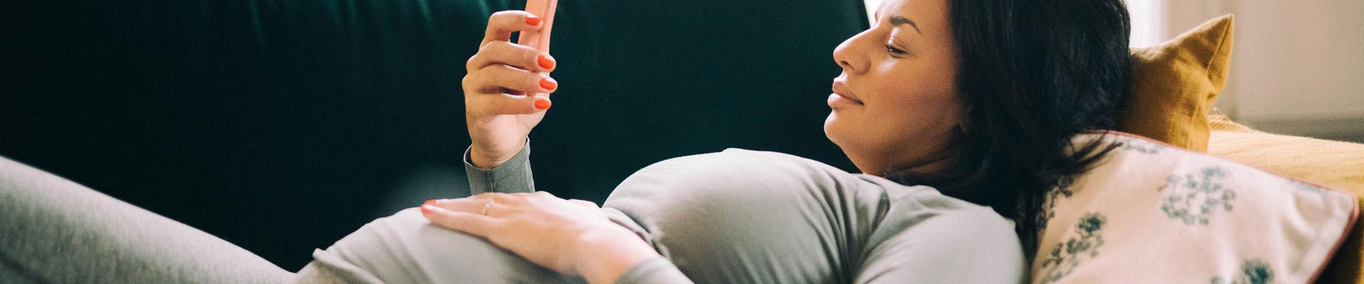 gravid kvinna ligger på soffa tittar på mobil