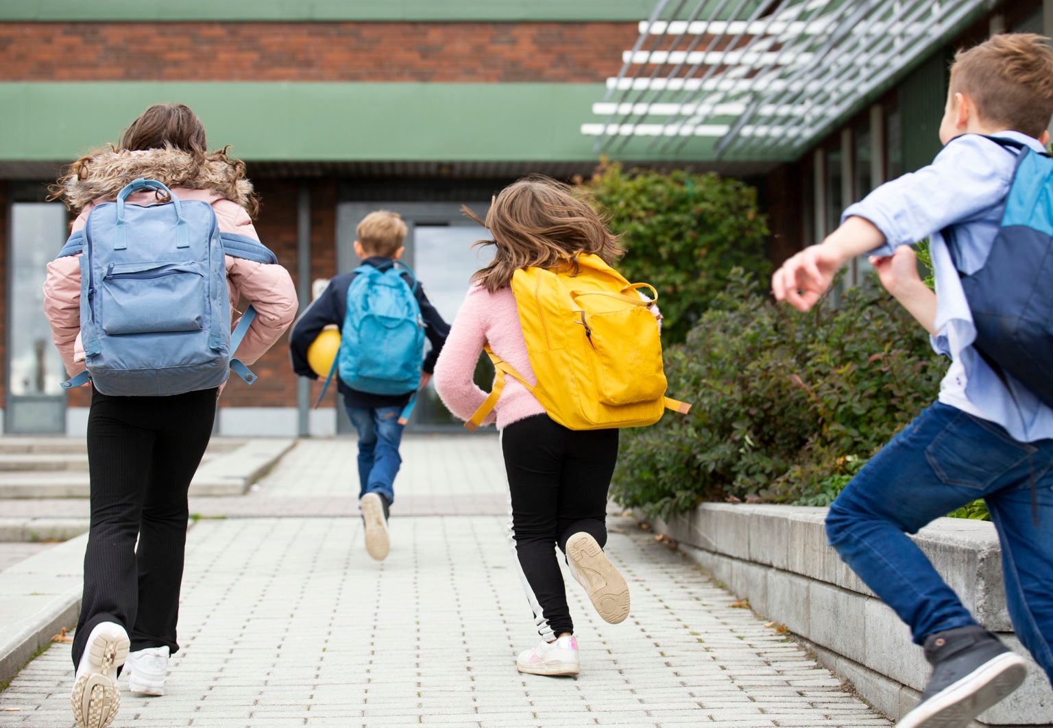 fyra barn med ryggsäckar springer till skolan