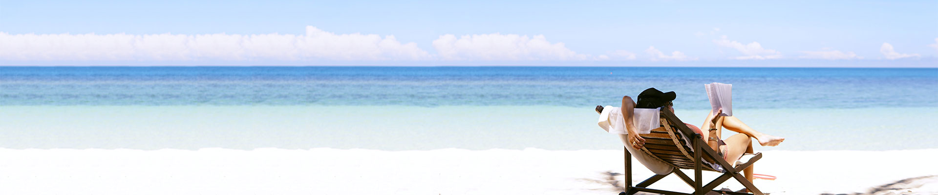kvinna sitter i solstol på sandstrand