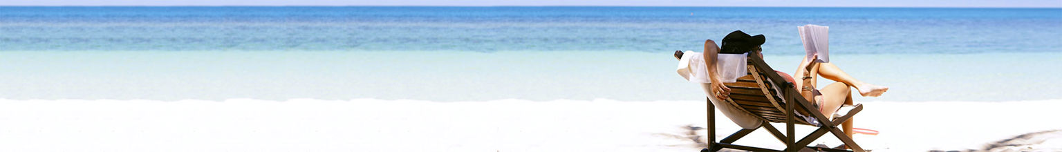 kvinna sitter i solstol på sandstrand