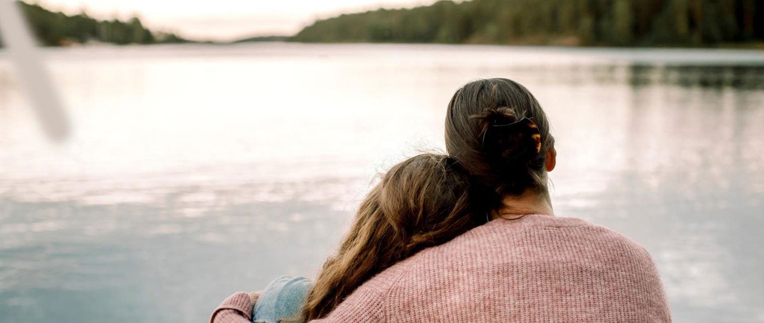 mamma håller om sin dotter vid en sjö